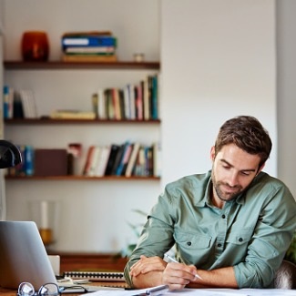 man writing at desk with laptop