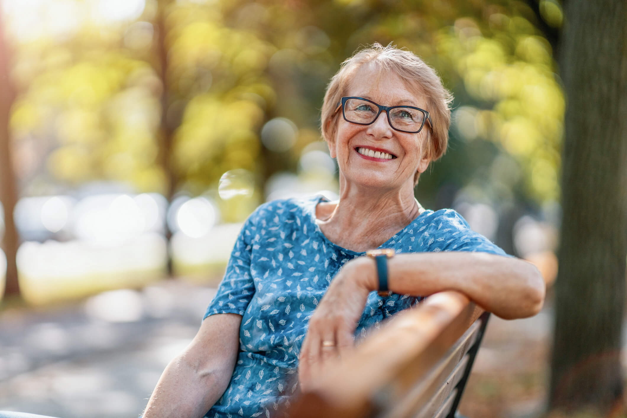 Older woman smiling outdoors on a park bench