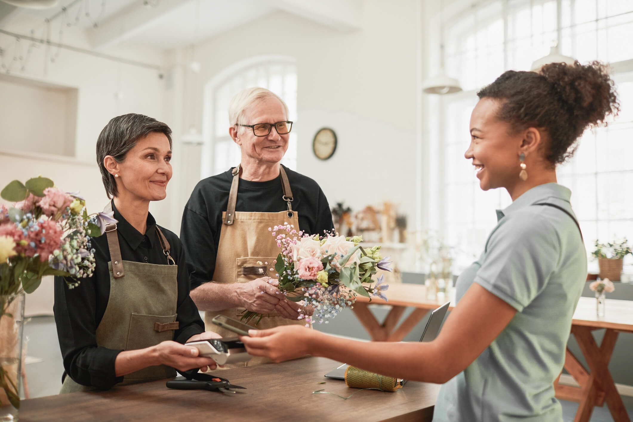 Couple handing bouquet to smiling customer while working in flower shop