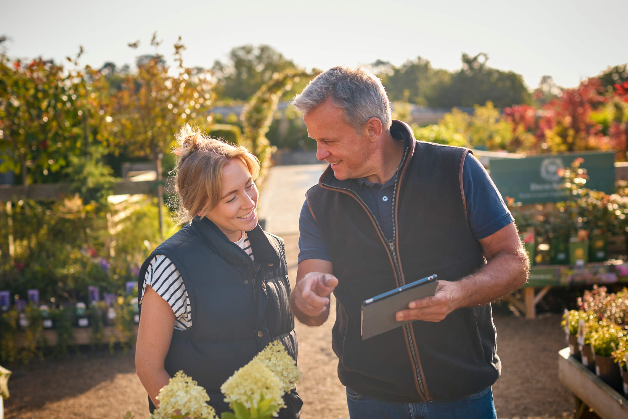People Working Outdoors In Garden Center Using Tablet
